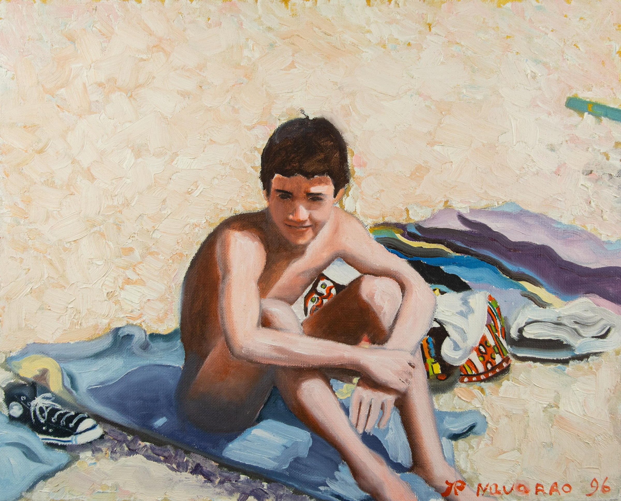 Un garçon assis sur une serviette sur la plage, entouré de vêtements colorés.